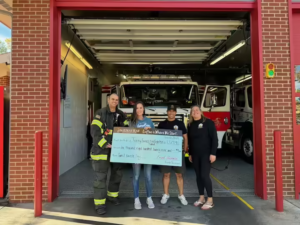 Four People holding a big check in the garage of a fire station