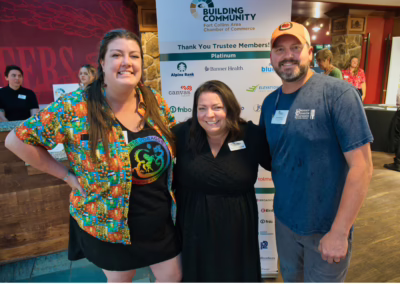 Three people smile and pose together at an indoor event in front of a “Fort Collins Area Chamber of Commerce” banner listing sponsors and members. The group appears friendly and casually dressed.