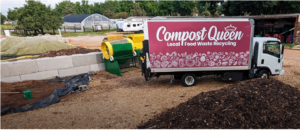 A truck with "Compost Queen: Local Food Waste Recycling" signage is parked at a composting facility, surrounded by mulch, compost piles, a green and yellow machine, and greenhouses in the background.